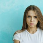 Angry young girl looking into camera on blue background