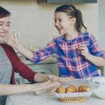 Young mother and her cute daughter have fun smearing nose each other with flour while cooking together in the kitchen on holidays. Family, food, home and people concept