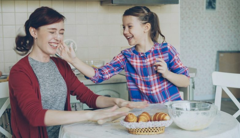 Young mother and her cute daughter have fun smearing nose each other with flour while cooking together in the kitchen on holidays. Family, food, home and people concept