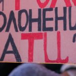Close-up of a hand holding a handmade cardboard protest sign lettered in red and black Ukrainian text asking who will be the voice of captives. The crowd behind is softly blurred, with hints of blue and yellow flags at a nighttime anti-war rally. Protesters rally in Times Square, New York City, on February 15, 2022, standing in solidarity with Ukraine and speaking out against the war at an anti-war demonstration. Photo: Olek Buzunov (@buzunov.photoart)